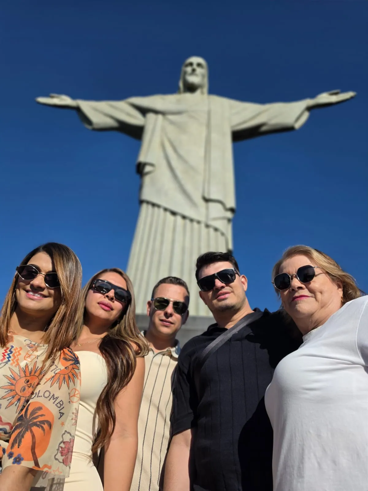 Visitors beneath Christ the Redeemer under a blue sky