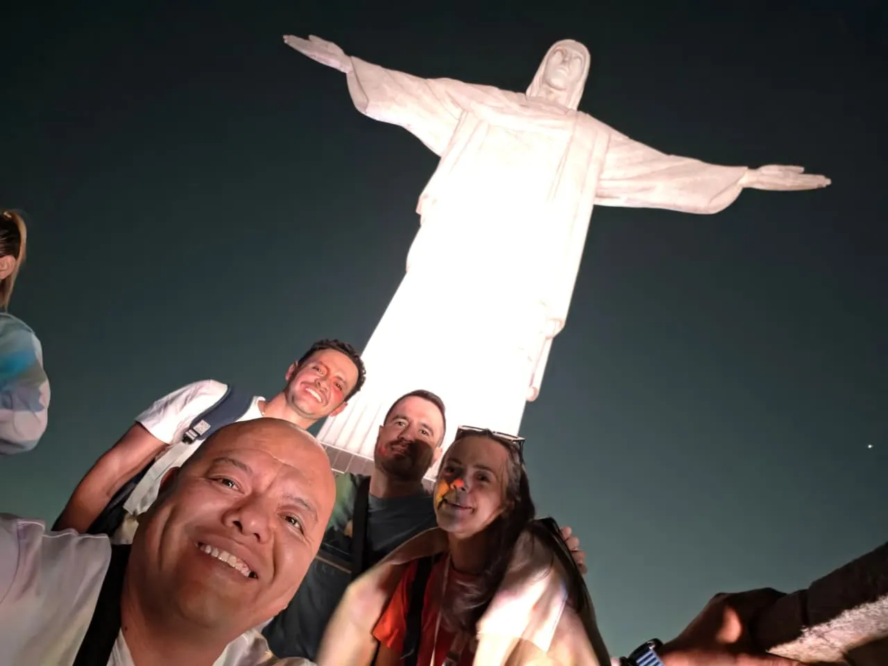 A group taking a selfie at night below the illuminated Christ the Redeemer